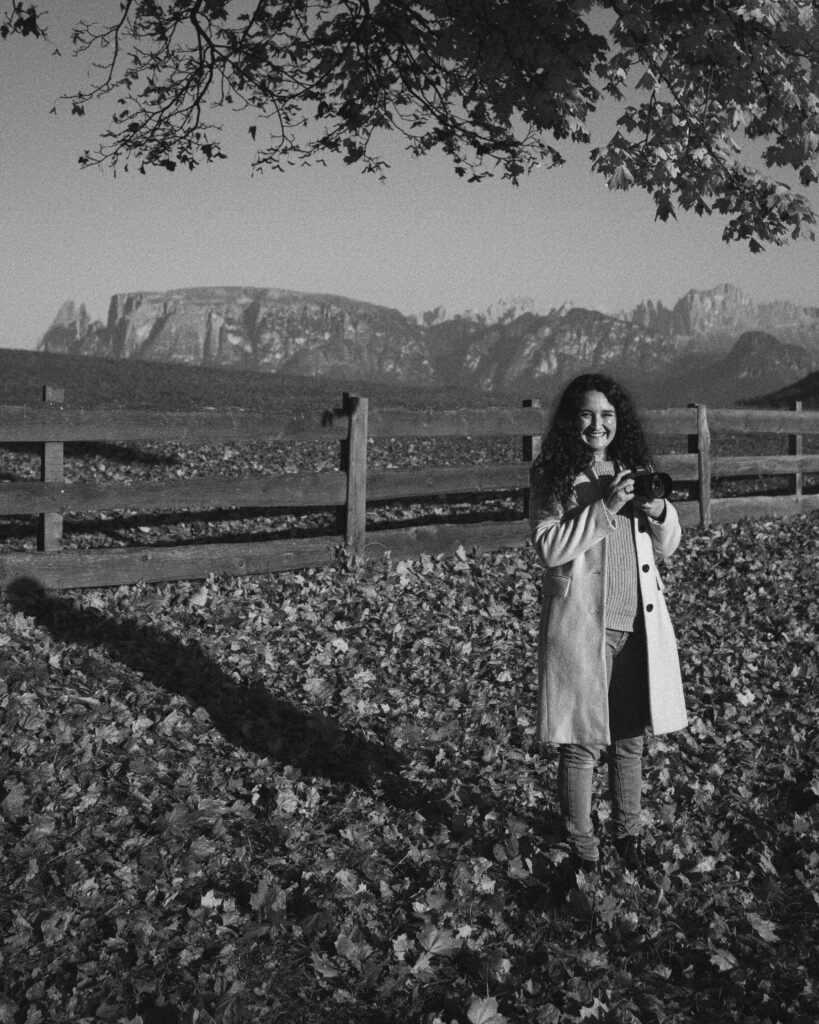 Anna Katharina Tonner mit Kamera in der Hand in herbstlicher Kulisse mit Schlern und Rosengarten im Hintergrund - schwarz/weiß